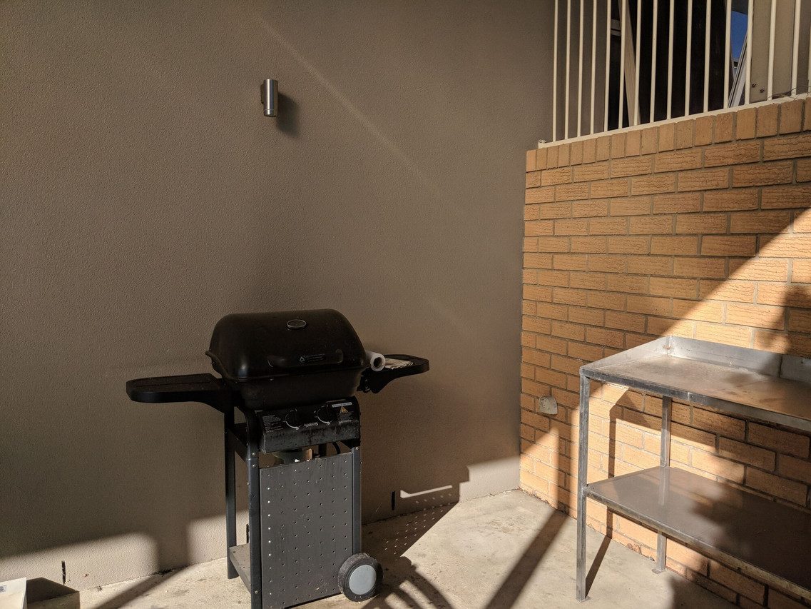 Covered barbecue area with a gas grill and stainless steel preparation bench